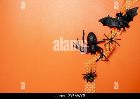 Un fond sur le thème d'Halloween avec un ruban orange, des araignées et une chauve-souris noire. Le fond est orange, ce qui ajoute à l'atmosphère effrayante du SC Banque D'Images