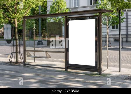 Maquette blanche vierge de panneau vertical d'arrêt de bus devant une rue vide. Visionneuse de publicité extérieure sur le trottoir Banque D'Images