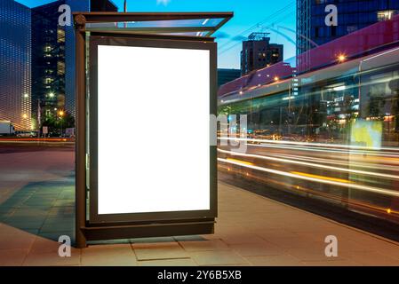 Maquette blanche vierge pour la publicité de bannière verticale à l'arrêt de bus la nuit. Panneau d'affichage des médias publics avec des traînées lumineuses à longue exposition Banque D'Images