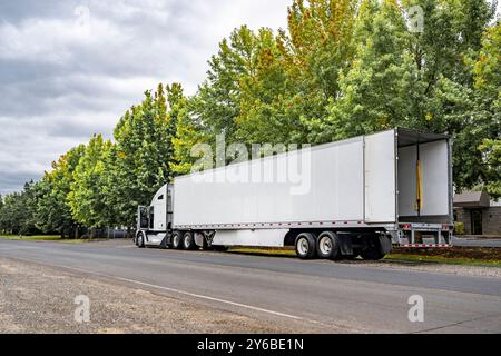 Semi-remorque grand engin de transport industriel longue portée blanche avec cabine allongée pour le repos du conducteur de camion et semi-remorque de fourgonnette sèche à porte arrière ouverte debout sur Banque D'Images