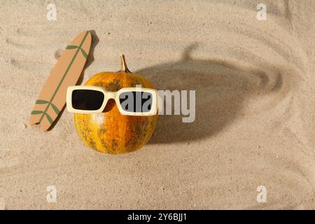 Citrouille d'Halloween, planche de surf et lunettes de soleil sur sable Banque D'Images