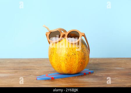 Citrouille d'Halloween dans des lunettes de soleil avec planche de surf sur une table en bois sur fond bleu Banque D'Images