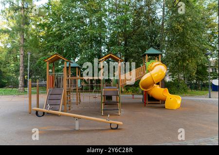 Parc lumineux avec structures d'escalade et toboggan entouré d'arbres luxuriants. Banque D'Images