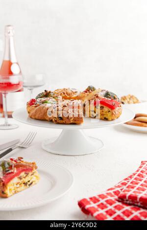 Un gâteau en forme de couronne avec des fruits confits et des noix sur un support à gâteau, avec des verres à vin en arrière-plan Banque D'Images