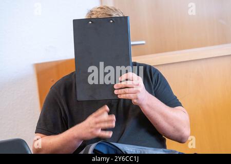 Rostock, Allemagne. 25 septembre 2024. L'accusé tient un bloc-notes devant son visage dans la salle d'audience du tribunal de district. Un an après un accident dramatique d'une moissonneuse-batteuse à Hohen Luckow (district de Rostock), un homme de 26 ans doit répondre de lésions corporelles par négligence au tribunal de district de Rostock. L'accusé est un collègue de l'agriculteur de 25 ans, qui a perdu les deux jambes dans l'accident. Crédit : Stefan Sauer/dpa/Alamy Live News Banque D'Images