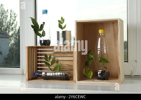 Concept de recyclage. Boîte en métal, bouteilles en plastique et caisses en bois avec des plantes sur le rebord de la fenêtre Banque D'Images