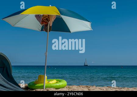 Un parasol coloré a été planté dans le sable blanc de Su Giudeu, Sardaigne, Italie, avec un voilier en arrière-plan Banque D'Images