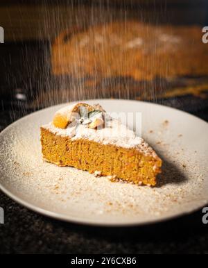 Une tranche de gâteau de carotte saupoudrée de sucre en poudre, garnie de tranches d'orange et de feuilles de menthe sur une assiette blanche. Banque D'Images