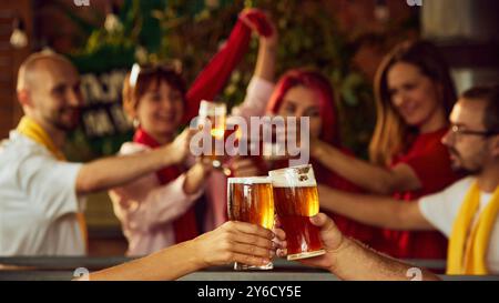 Deux amis portent un toast à des verres de bière, tandis que les fans flous en arrière-plan soulèvent les leurs en célébrant, capturant l'excitation de la grande victoire. Les encouragements résonnent Banque D'Images