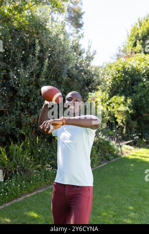 Lancer le football, homme afro-américain profitant de l'activité de plein air dans le jardin arrière avec des arbres Banque D'Images