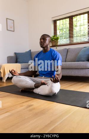 A la maison, méditant sur tapis de yoga, homme afro-américain pratiquant la pleine conscience dans le salon Banque D'Images