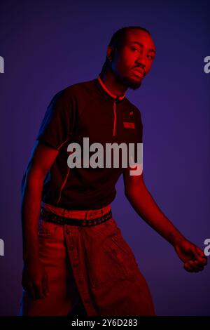 Un jeune homme dans des vêtements à la mode se tient en toute confiance dans un studio, illuminé par des couleurs néon saisissantes. Banque D'Images