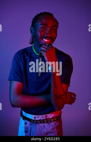 Un jeune homme afro-américain met en valeur son style unique tout en posant sous un éclairage au néon vibrant. Banque D'Images