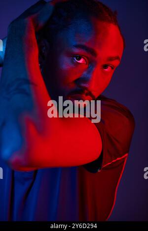 Un jeune homme afro-américain présente sa tenue élégante tout en saisissant une pose dynamique dans un studio éclairé au néon. Banque D'Images