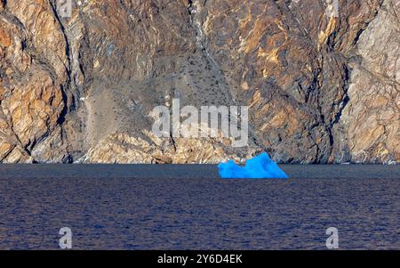 Iceberg bleu au crépuscule dans le fjord de Dickson, dans le parc national du nord-est du Groenland. Les formations rocheuses colorées s'élèvent de l'eau calme du fjord pour former un Banque D'Images