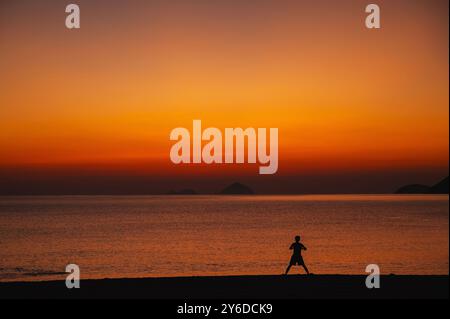 Silhouette d'un homme asiatique faisant des exercices sur la plage au bord de la mer le matin au lever du soleil en été Banque D'Images