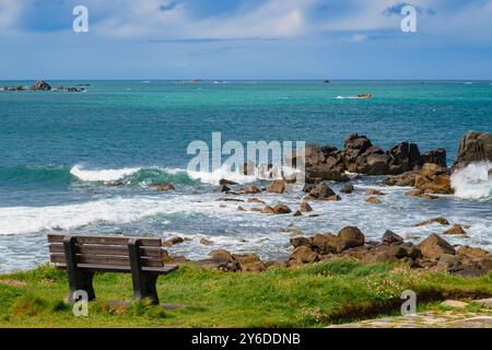 La baie de Grand Havre et un banc vide par le sentier côtier autour du promontoire de Chouet avec des vagues s'écrasant sur les rochers. Guernesey, Îles Anglo-Normandes, Royaume-Uni, Grande-Bretagne Banque D'Images