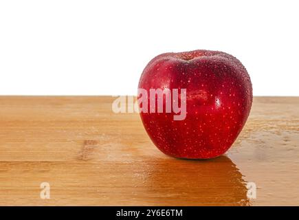 Pomme rouge avec des gouttelettes d'eau sur une planche de bois clair. Gros plan mettant en valeur la fraîcheur et le contraste de couleurs éclatant sur la surface naturelle Banque D'Images