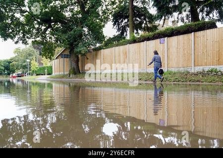 Une femme marche le long d'un sentier près d'une route inondée à Harrold, Bedfordshire. Un avertissement météorologique jaune pour des pluies plus abondantes a été émis pour jeudi, alors que le Royaume-Uni se remet des inondations soudaines qui ont vu des maisons endommagées et les déplacements perturbés. Date de la photo : mercredi 25 septembre 2024. Banque D'Images