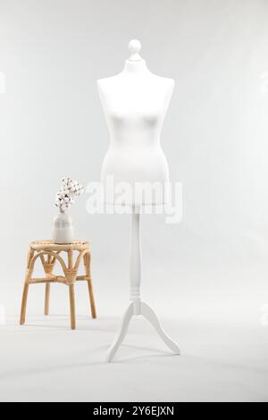 Un mannequin féminin sur support, tabouret et vase avec des fleurs de coton sur fond clair Banque D'Images