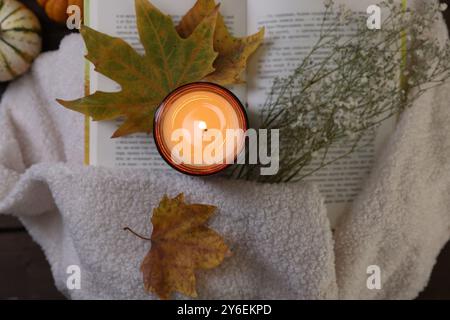 Bougie allumée, livre ouvert, chandail et décor d'automne sur la table, vue de dessus Banque D'Images