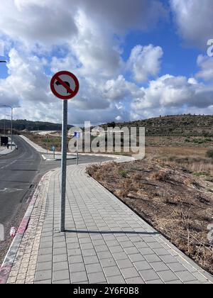 Un panneau routier No Left Turn se trouve sur un trottoir le long d'une route rurale sous un ciel partiellement nuageux. Le paysage derrière présente des collines ondulantes et des champs ouverts. Banque D'Images