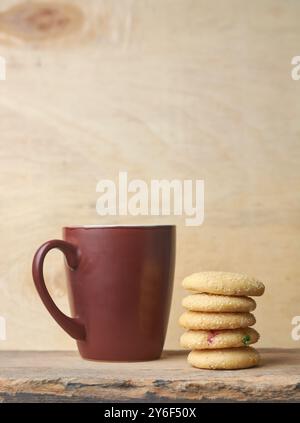 biscuits au sucre empilés sur le dessus de table en bois avec tasse ou tasse en arrière-plan, biscuits sucrés cuits au four avec texture croustillante et saveur de beurre, espace de copie Banque D'Images