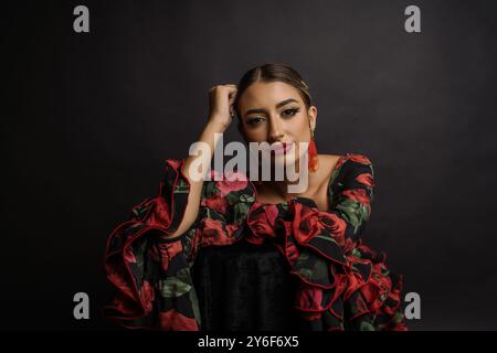 Une jeune femme en robe de flamenco traditionnelle avec des motifs floraux rouges et verts sur un fond sombre. Banque D'Images