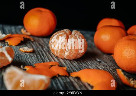 gros plan de quelques délicieuses mandarines, l'une d'entre elles pelée, sur une table en bois rustique gris, à côté de quelques pelures de mandarine Banque D'Images
