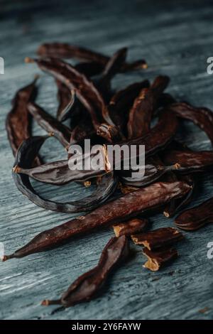 quelques gousses de caroube mûres sur une table en bois rustique gris Banque D'Images