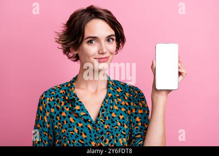 Photo de fille optimiste habillée chemise élégante présentant la conception d'interface utilisateur sur l'écran de smartphone espace vide isolé sur fond de couleur rose Banque D'Images