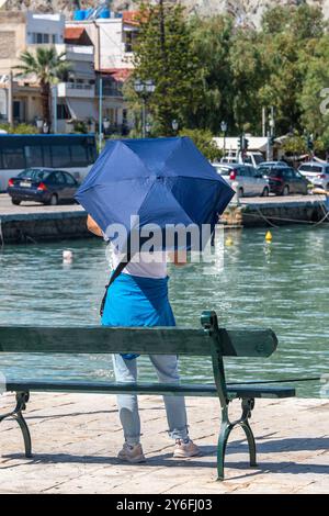 femme debout seule sur le côté du port à l'aide d'un parasol pour se faire de l'ombre du soleil méditerranéen chaud de l'été Banque D'Images