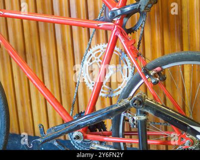 Le vélo rouge s'appuie contre un mur de bois, mettant en valeur ses engrenages et sa chaîne. La sensation vintage ajoute un style urbain, évoquant la liberté et l'aventure Banque D'Images