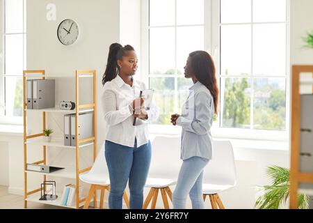 Collègues afro-américaines parlant, amies de bureau, femmes rencontrées dans le hall de bureau bavardant Banque D'Images