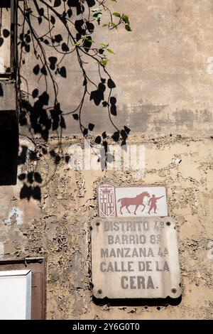 Un panneau de rue altéré identifie la Placa de la Calle de la Cera dans le quartier animé du Raval de Barcelone sous des branches verdoyantes. Banque D'Images