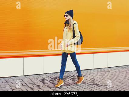 Mode jolie femme blonde marchant dans la ville sur un fond coloré orange Banque D'Images