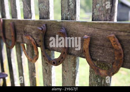 Une collection de vieux fers à cheval rouillés de chance sont accrochés à une clôture en bois rustique. Banque D'Images