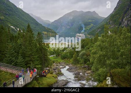 Un paysage impressionnant avec une cascade déchaînée, entouré de montagnes verdoyantes et de forêts, avec un bateau de croisière, Mein Schiff 6, sur un sentier de randonnée dans le fjord Banque D'Images