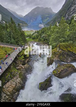 Un paysage impressionnant avec une cascade déchaînée, entouré de montagnes verdoyantes et de forêts, avec un bateau de croisière, Mein Schiff 6, sur un sentier de randonnée dans le fjord Banque D'Images