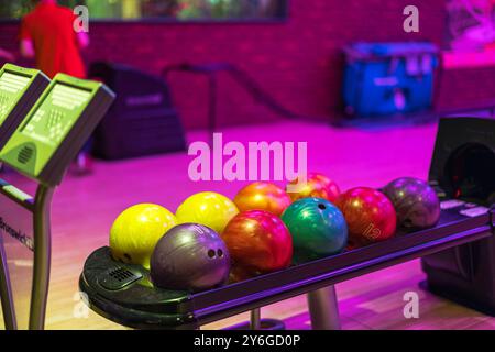 Boules de bowling colorées sur rack au système de retour de balle dans la piste de bowling avec tableaux de bord électroniques. Banque D'Images