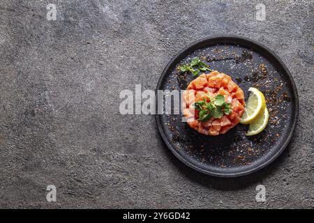 Nourriture, saumon cru, salade d'oignons violets d'avocat servie en anneau culinaire sur assiette noire. Fond de béton noir Banque D'Images