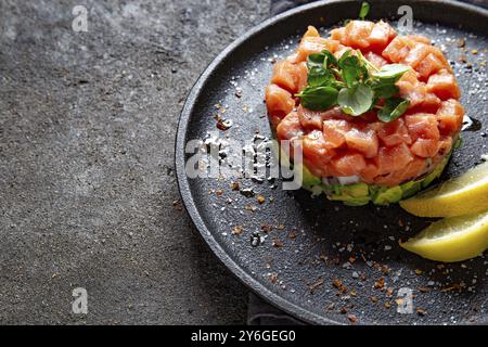 Nourriture, saumon cru, salade d'oignons violets d'avocat servie en anneau culinaire sur assiette noire. Fond de béton noir Banque D'Images