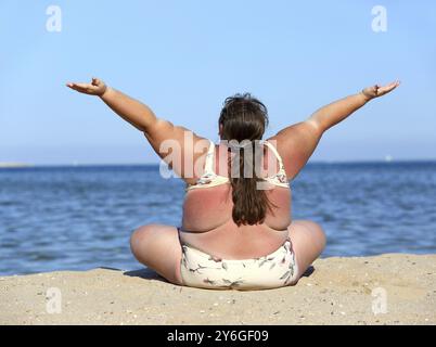 Femme en surpoids assise sur la plage avec les mains vers le haut Banque D'Images