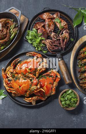 Nourriture, nourriture, ensemble de plats de fruits de mer. Crabes, poulpes, calmars et crevettes tigrées sur des casseroles et des assiettes en fonte sur fond noir. Vue de dessus Banque D'Images