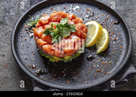 Nourriture, saumon cru, salade d'oignons violets d'avocat servie en anneau culinaire sur assiette noire. Fond de béton noir Banque D'Images