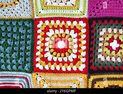 Fragment de couverture en Granny Square crocheté avec rouge, blanc, orange, jaune, vert, bleu et fil avec différents motifs. Banque D'Images