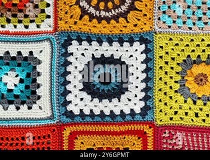 Fond de couverture carrée multicolore Granny crocheté avec du fil blanc, bleu foncé, rouge, jaune, vert et orange avec différents motifs. Banque D'Images