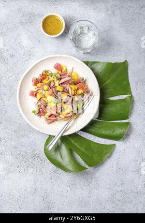 Nourriture, salade tropicale de thon tahitien tahitien et mangue sur assiette blanche sur feuille de monstera tropicale Banque D'Images