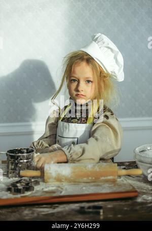 Une fille portant un chapeau de chef est assise à une table. Banque D'Images