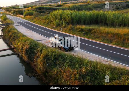 Une voiture garée à côté d'une rivière tranquille sur une route sinueuse pendant l'heure dorée dans la campagne. Banque D'Images